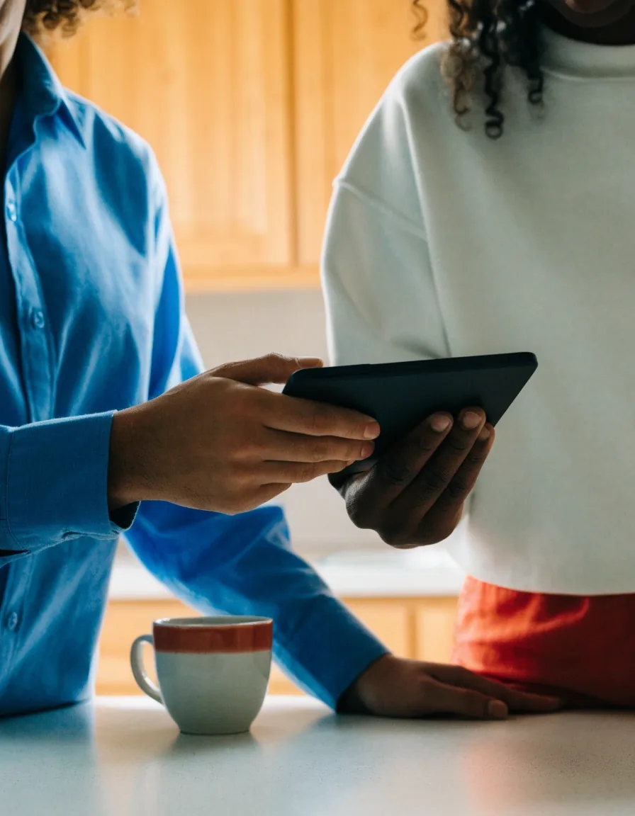 Two people reviewing booking details together on a tablet at a kitchen counter