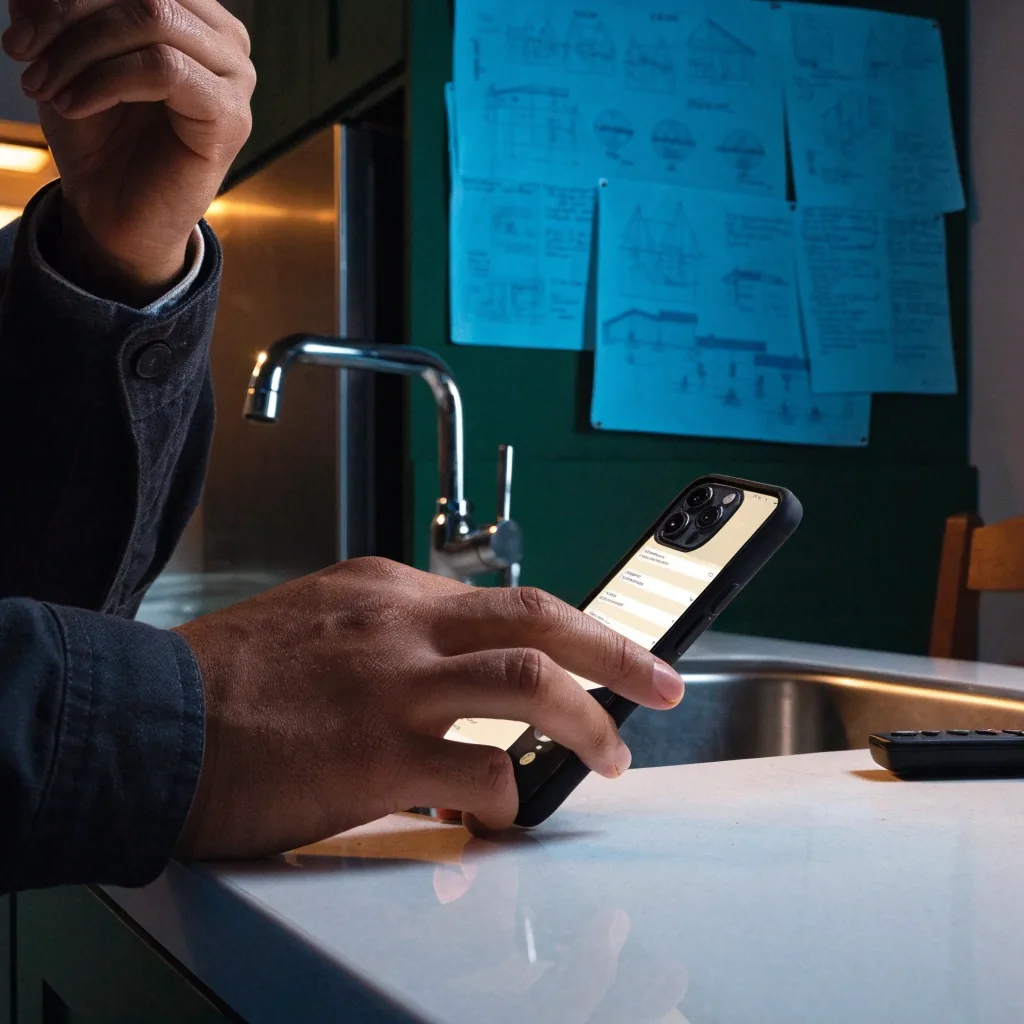 Hands entering booking details on a phone at a kitchen counter